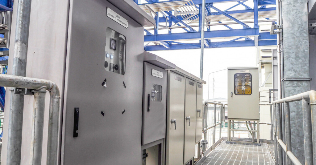 A walkway and railing of a row of local control boxes and electric enclosures in an industrial setting.