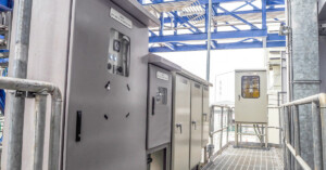 A walkway and railing of a row of local control boxes and electric enclosures in an industrial setting.