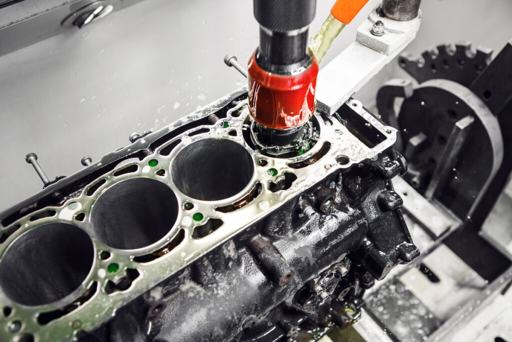 A CNC machine smoothing out the cylinder walls of an engine with a red cylindrical attachment used for boring.