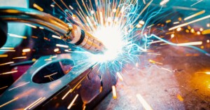 An arc welder creating a radiating point of light from its electric arc connecting with a metal joint.